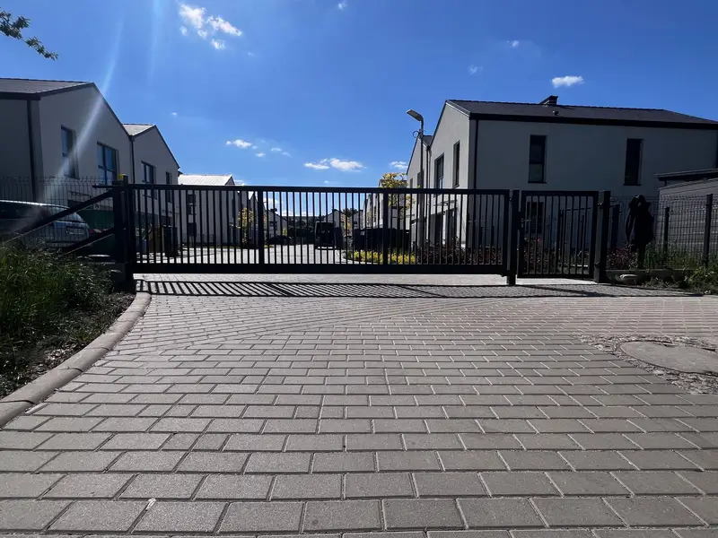 Brama z pionowych prętów na końcu podjazdu z kostki na osiedlu