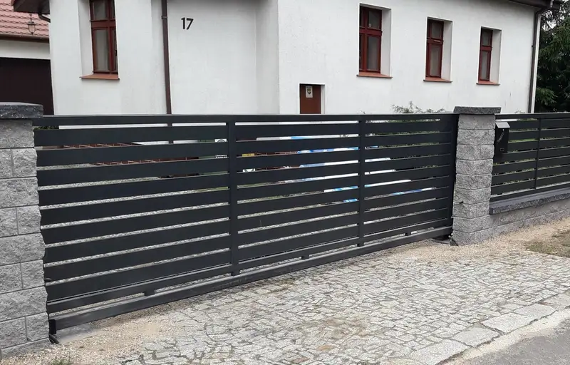 Antracytowa brama przesuwna z poziomych profili przy wjeździe na posesję