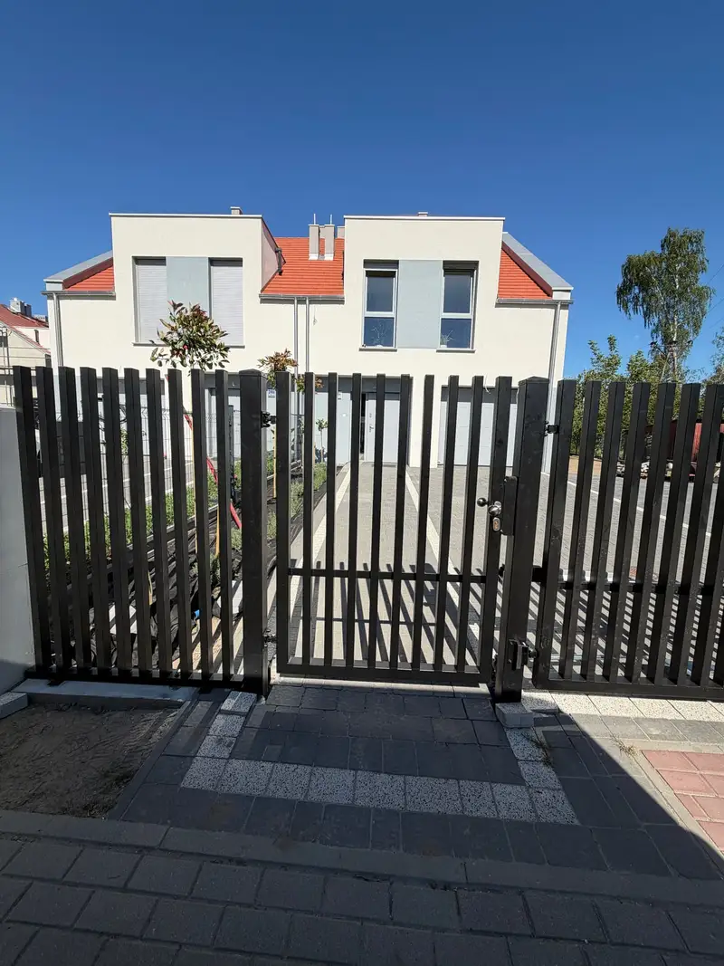 Czarna furtka i brama z pionowych profili przed jasnym bliźniakiem