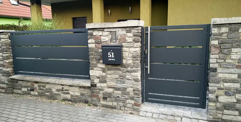 Grafitowa furtka i przęsło między słupkami z kamienia z tabliczką numeru