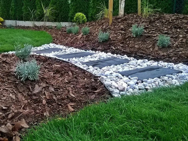 Ścieżka z otoczaków i płyt wijąca się między trawnikiem a korą